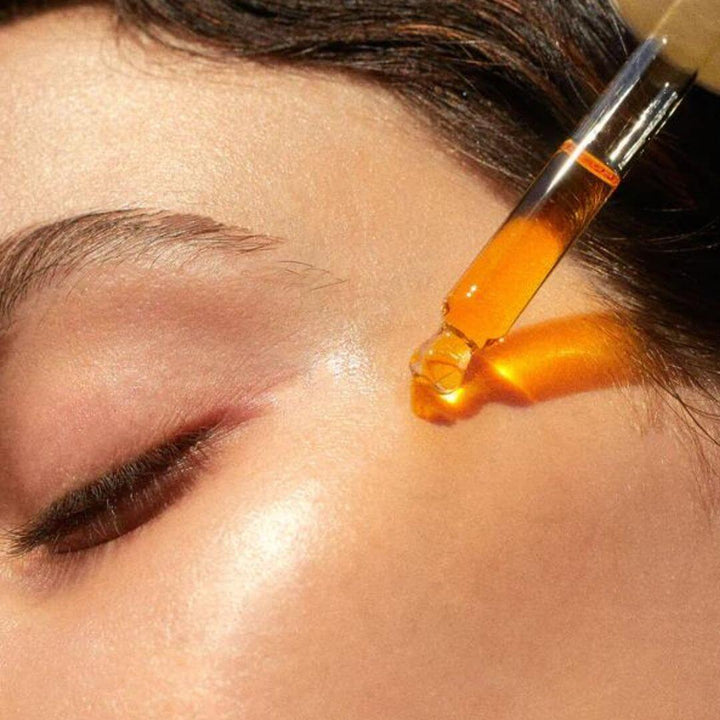 Woman applying a drop of Brilliance Serum with Vitamin C, capturing the essence of its silky texture for a radiant skincare experience