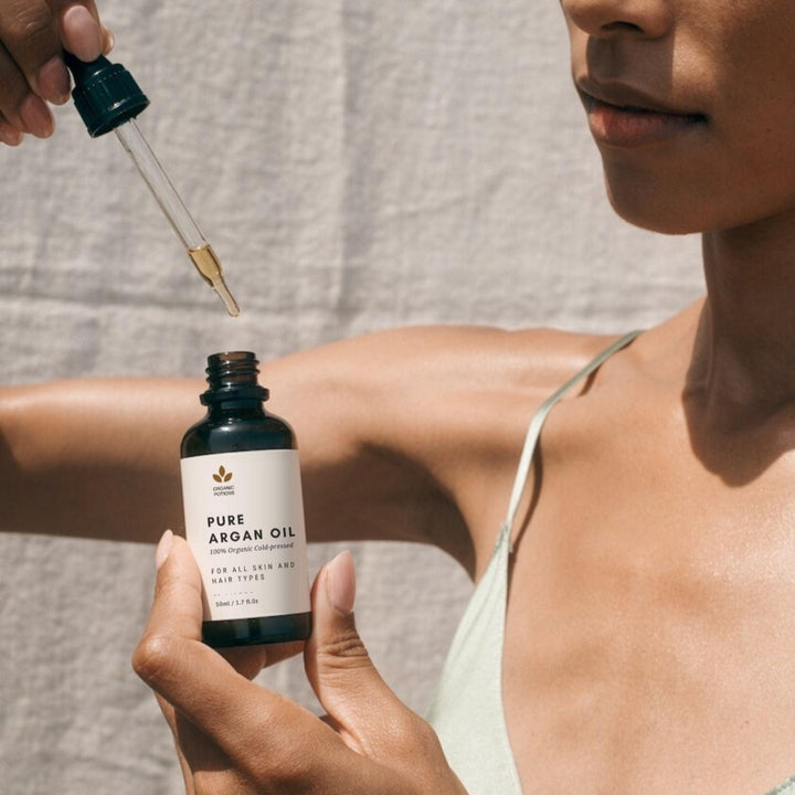 A woman holding a dropper with Organic Potions' Argan Oil, ready to apply the nourishing and hydrating benefits to her skin